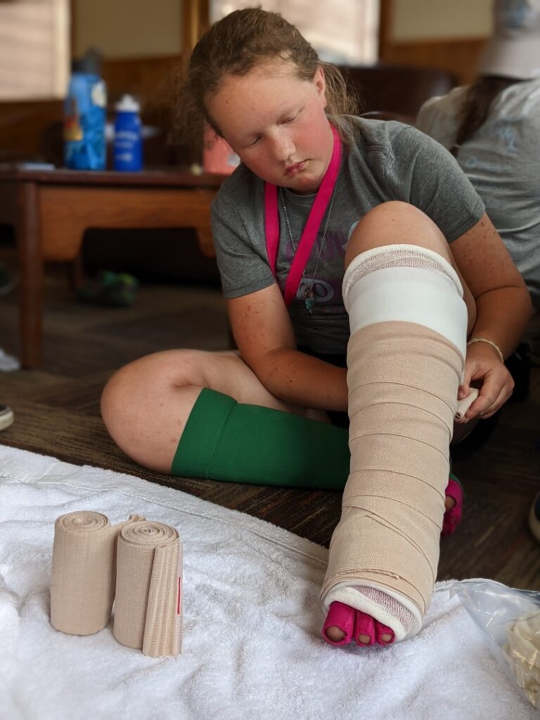 Maddy concentrates as she practices bandaging on her leg.