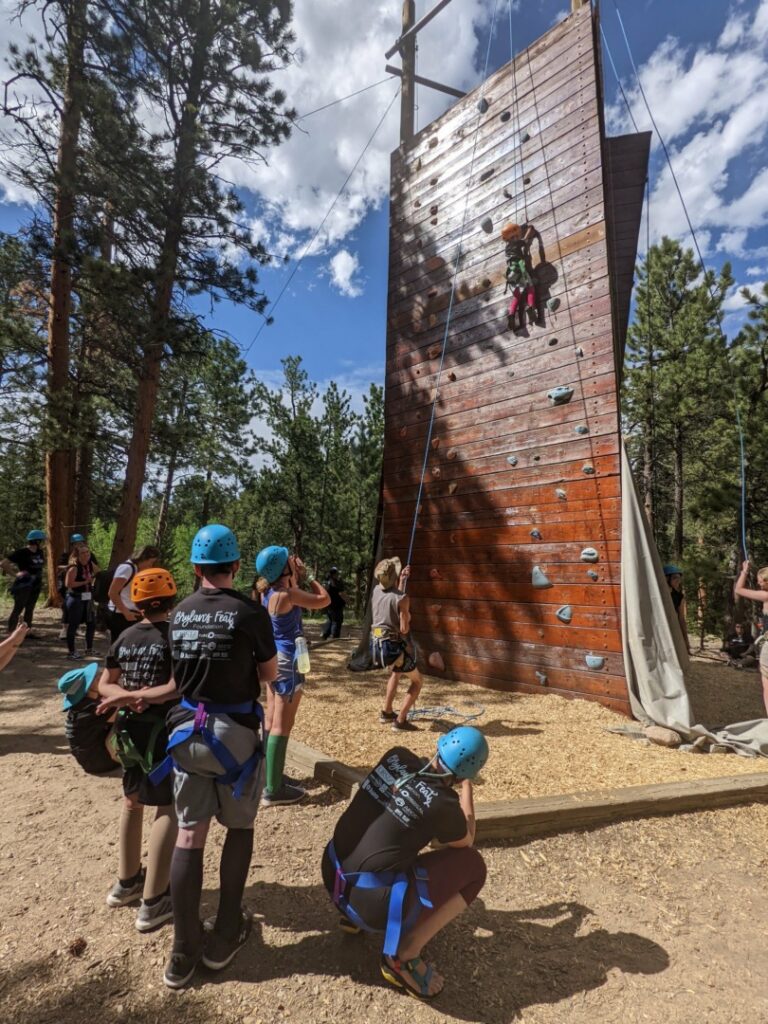Campers and family members look on as five-year-old Grayson scales the rock climbing wall.