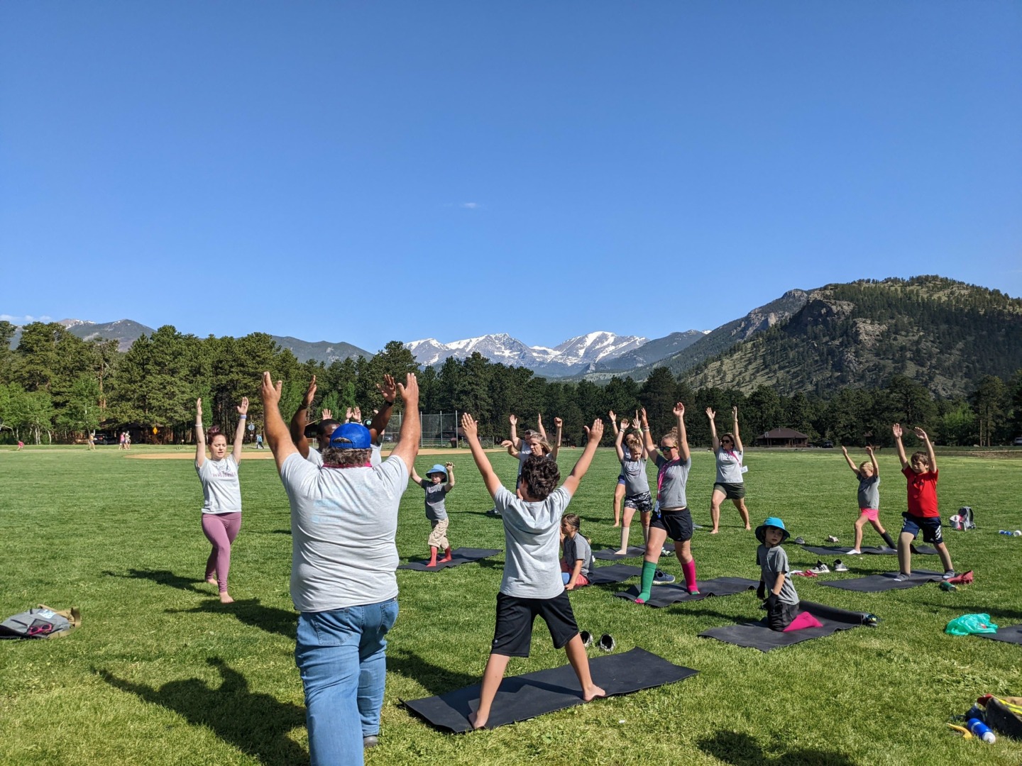 Campers and their families do yoga outside with the Rocky Mountains behind them.