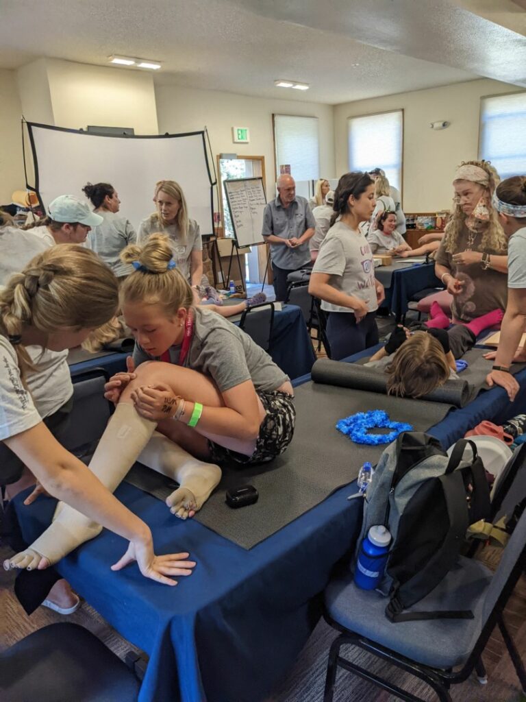 Campers, parents, and certified lymphedema therapists mill around during an educational session on manual lymphatic drainage.