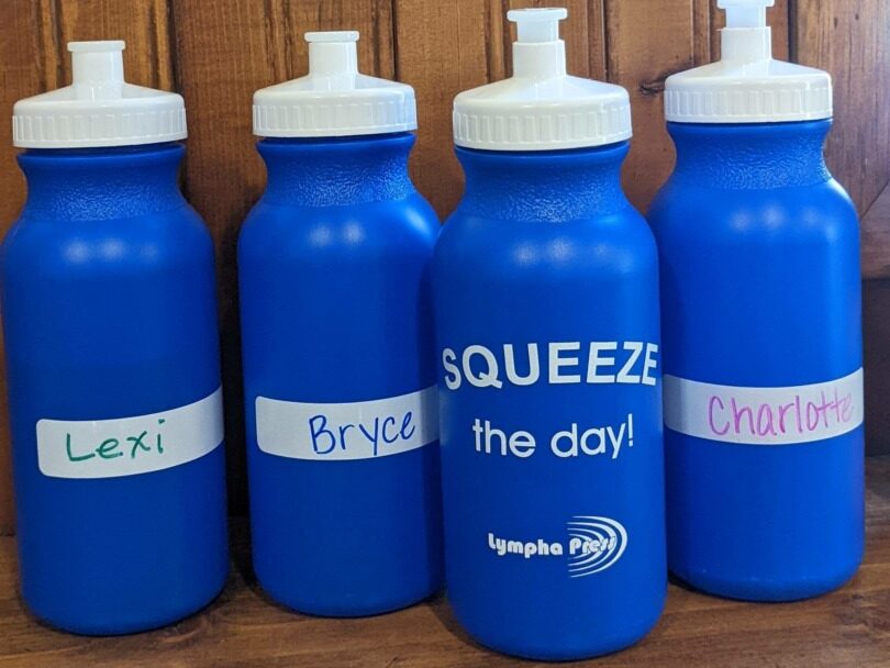 A row of Lympha Press reusable water bottles that say "Squeeze the Day"!