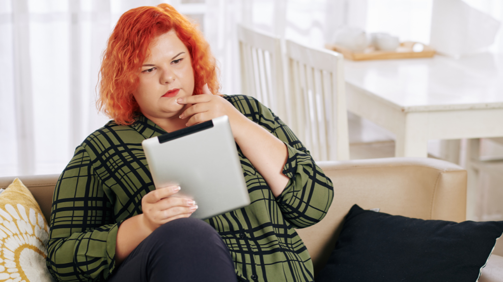 An overweight woman looks pensive and she reviews information on her tablet.