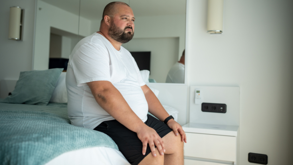 a man sits on the edge of his bed, looking distressed